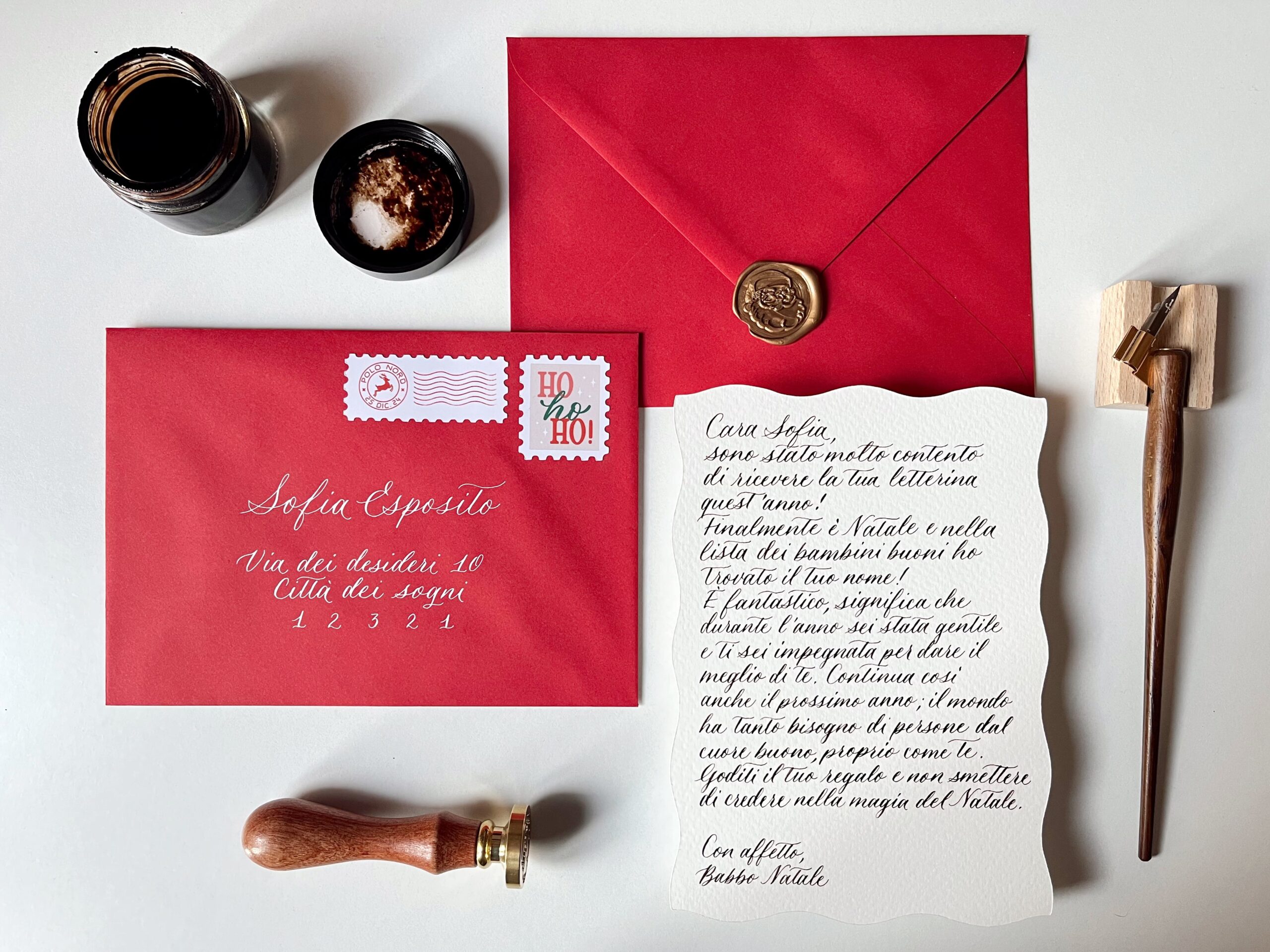 Foto di una lettera di risposta da Babbo Natale scritta a mano in calligrafia, con busta rossa e sigillo in ceralacca